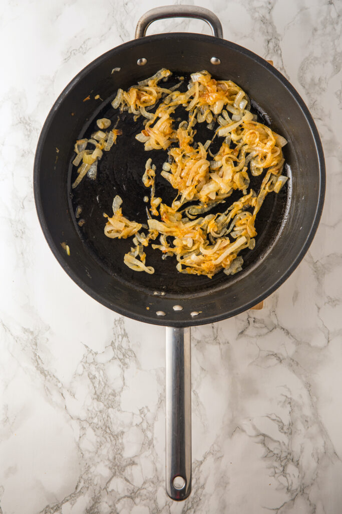 Sautéed onions in a black frying pan, reminiscent of the rich flavors found in French onion dip, rest elegantly on a marble countertop.