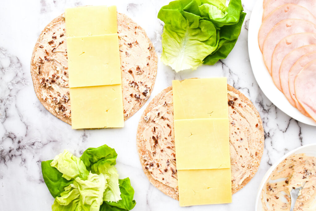 Two turkey pinwheel wraps rest on a marble surface, filled with cheese, crisp lettuce, and perfectly sliced meat.