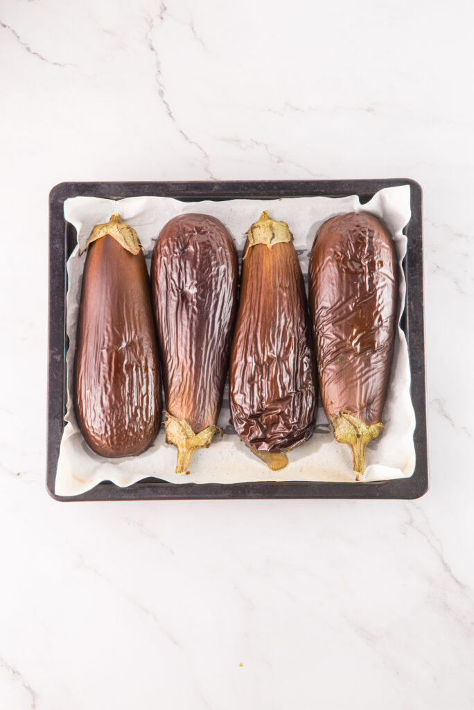 Four roasted eggplants on a baking tray lined with parchment paper.