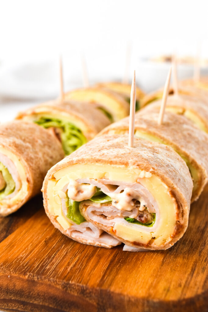 Close-up of sliced tortilla wraps with lettuce, turkey, and cheese, secured with toothpicks on a wooden board.