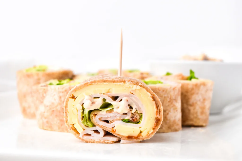 Close-up of a sliced turkey and cheese pinwheel sandwich with lettuce and a toothpick, arranged on a white plate.