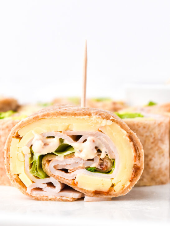 Close-up of a sliced turkey and cheese pinwheel sandwich with lettuce and a toothpick, arranged on a white plate.