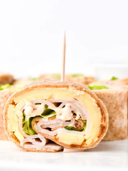 Close-up of a sliced turkey and cheese pinwheel sandwich with lettuce and a toothpick, arranged on a white plate.