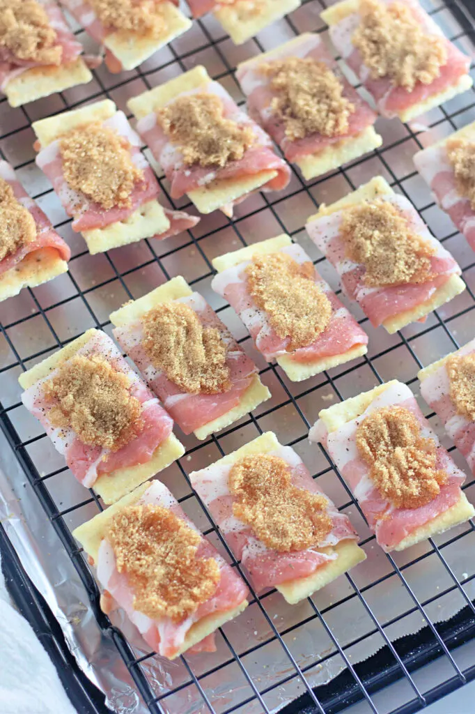 Crackers topped with prosciutto and brown sugar are arranged on a cooling rack lined with foil.